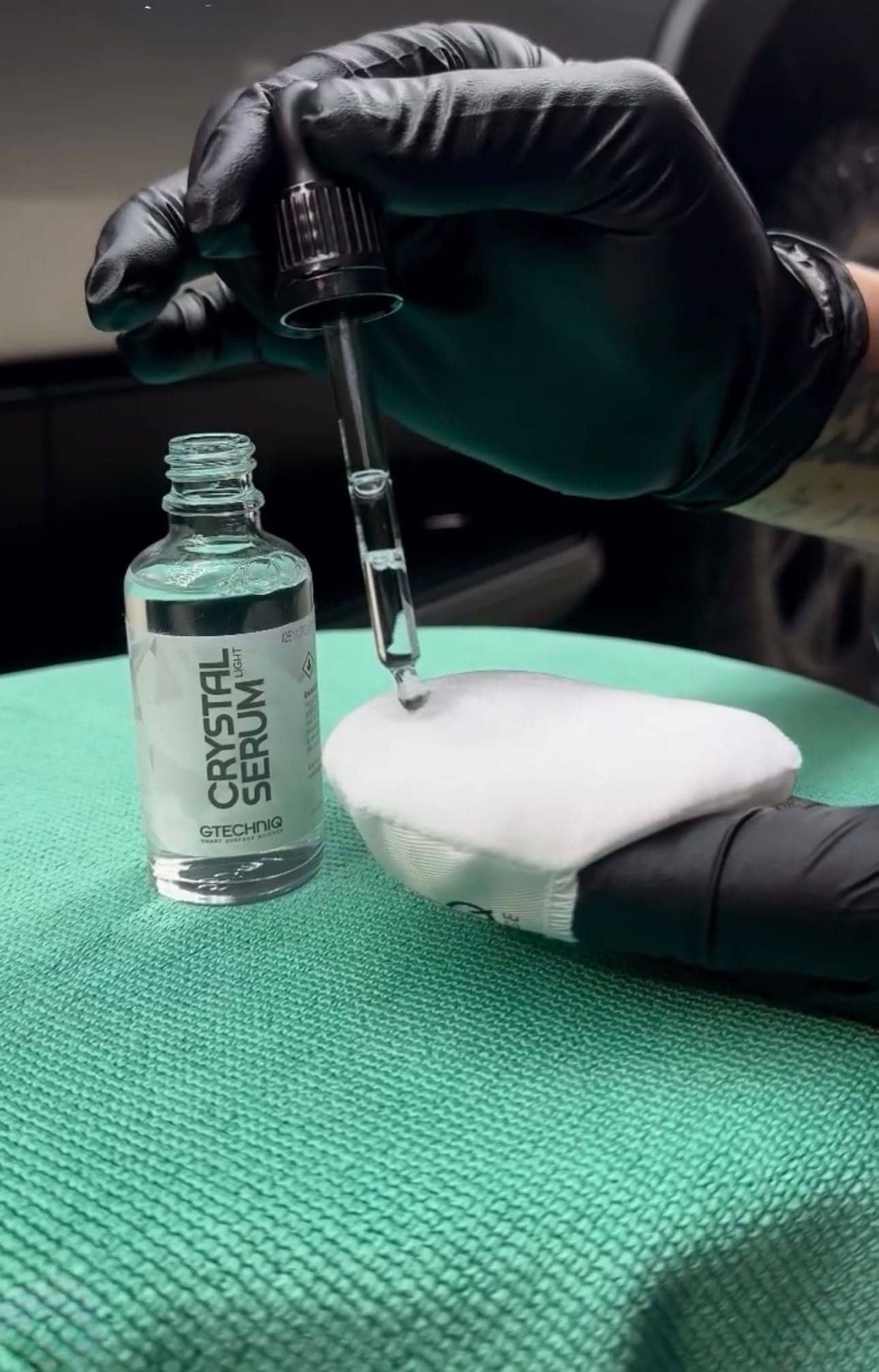 Gloved hand loading a ceramic coating applicator from a dropper bottle