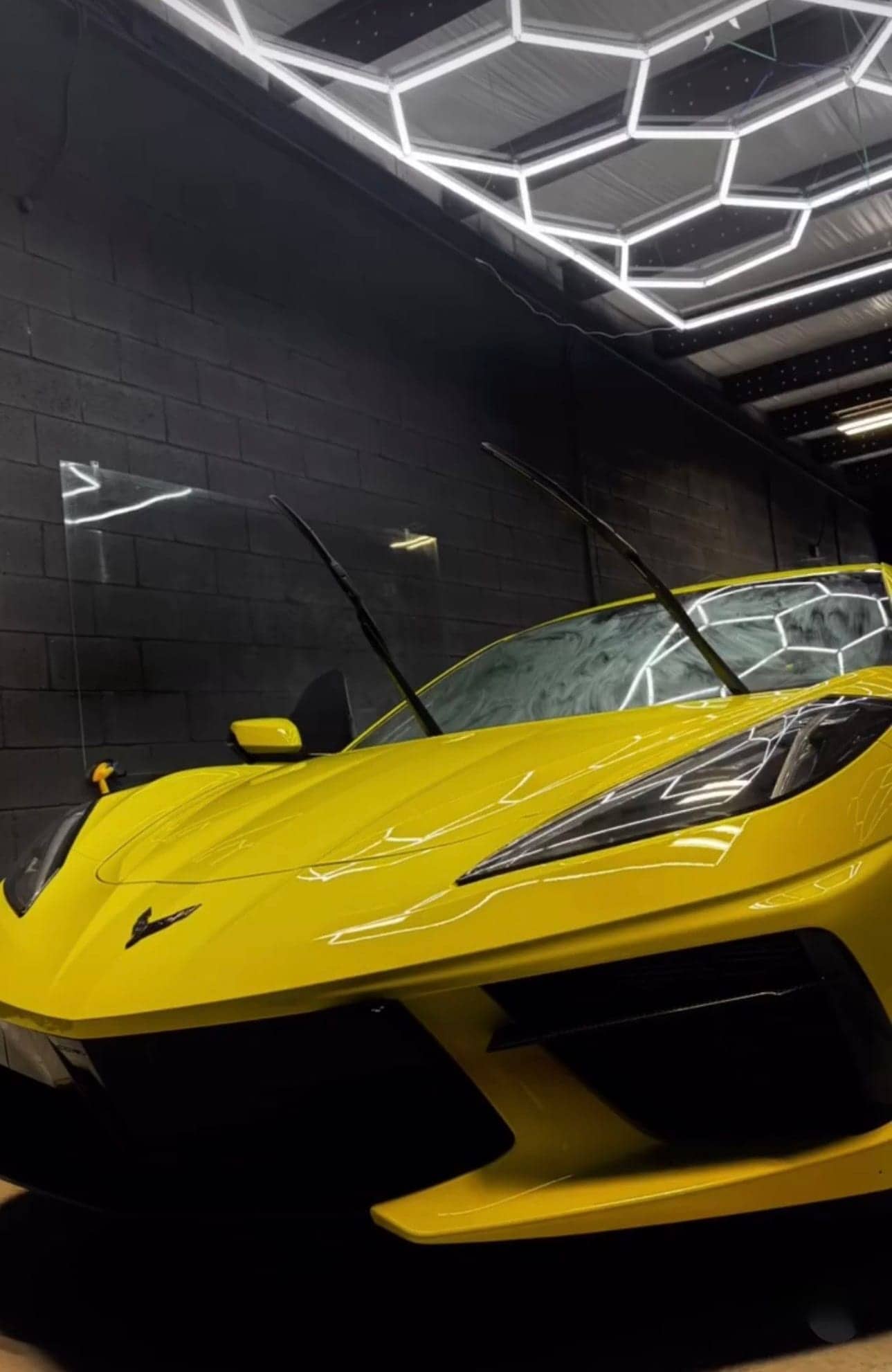 Yellow mid-engine Chevrolet Corvette under hexagon lights in the Equinox Tinting bay