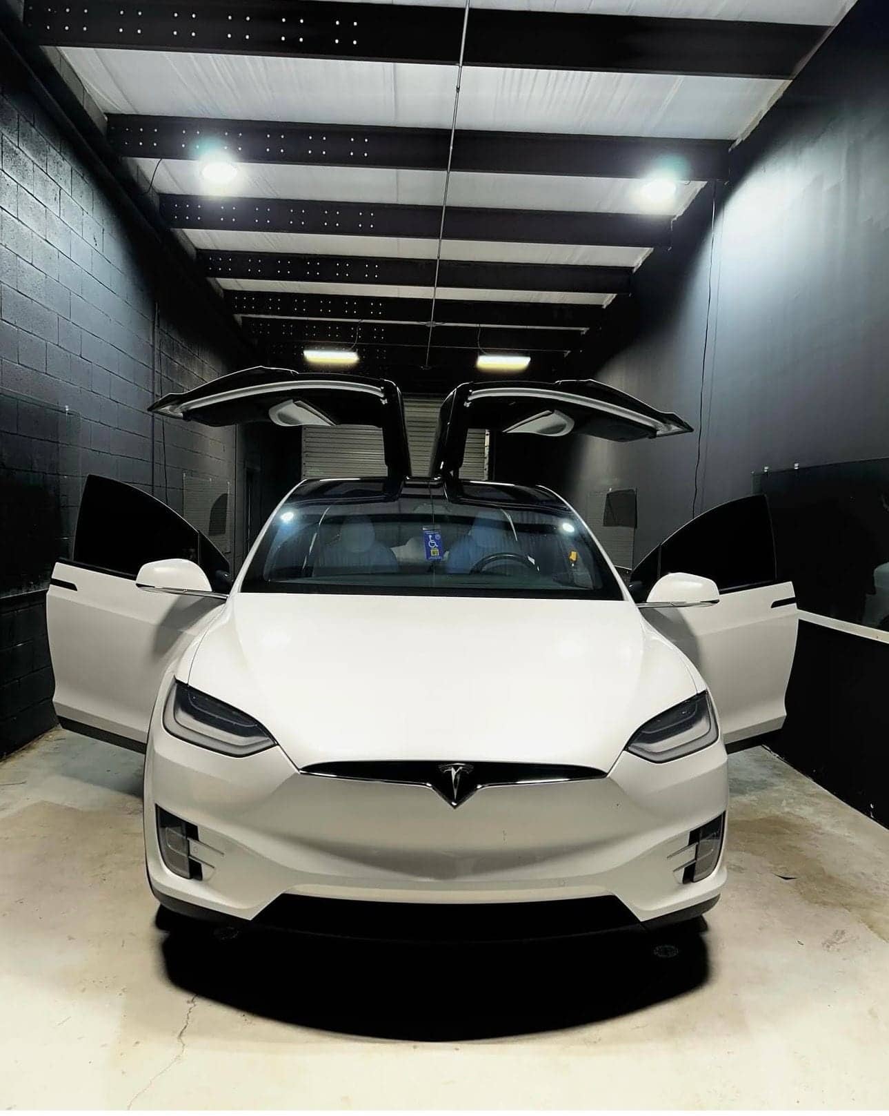 White Tesla Model X with its falcon-wing doors raised in the Equinox Tinting bay