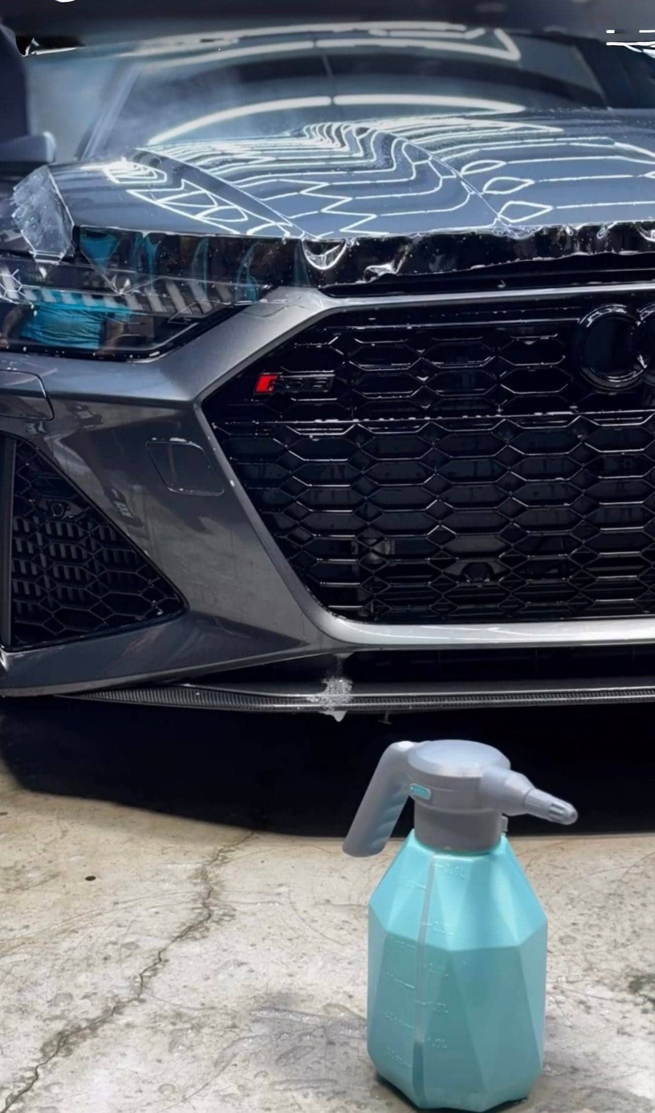 Gray Audi RS with film being installed over the front end, spray bottle on the floor