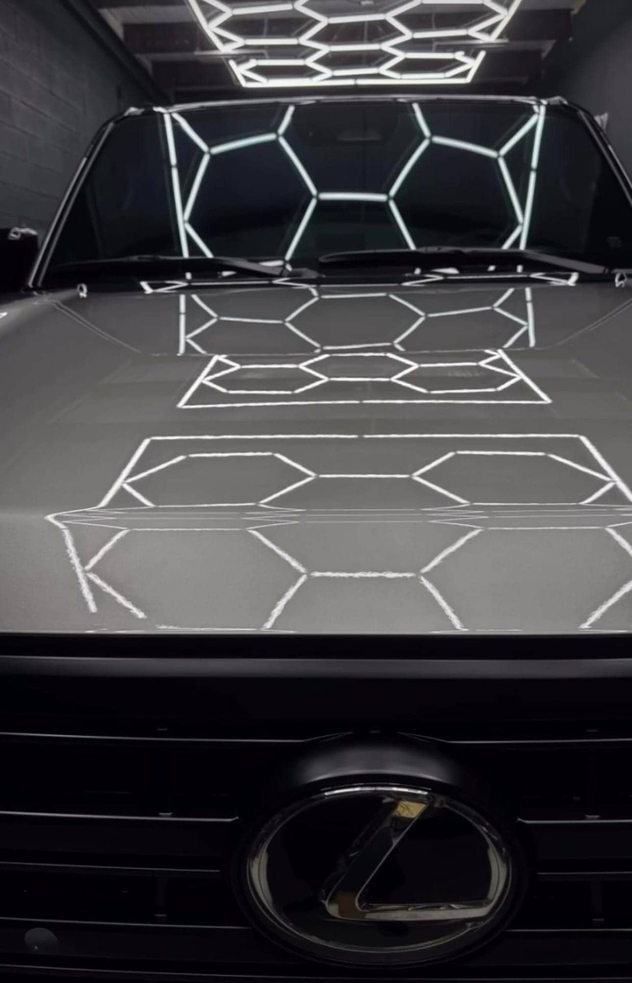 Hexagon studio lights reflected across the glossy hood of a dark Lexus
